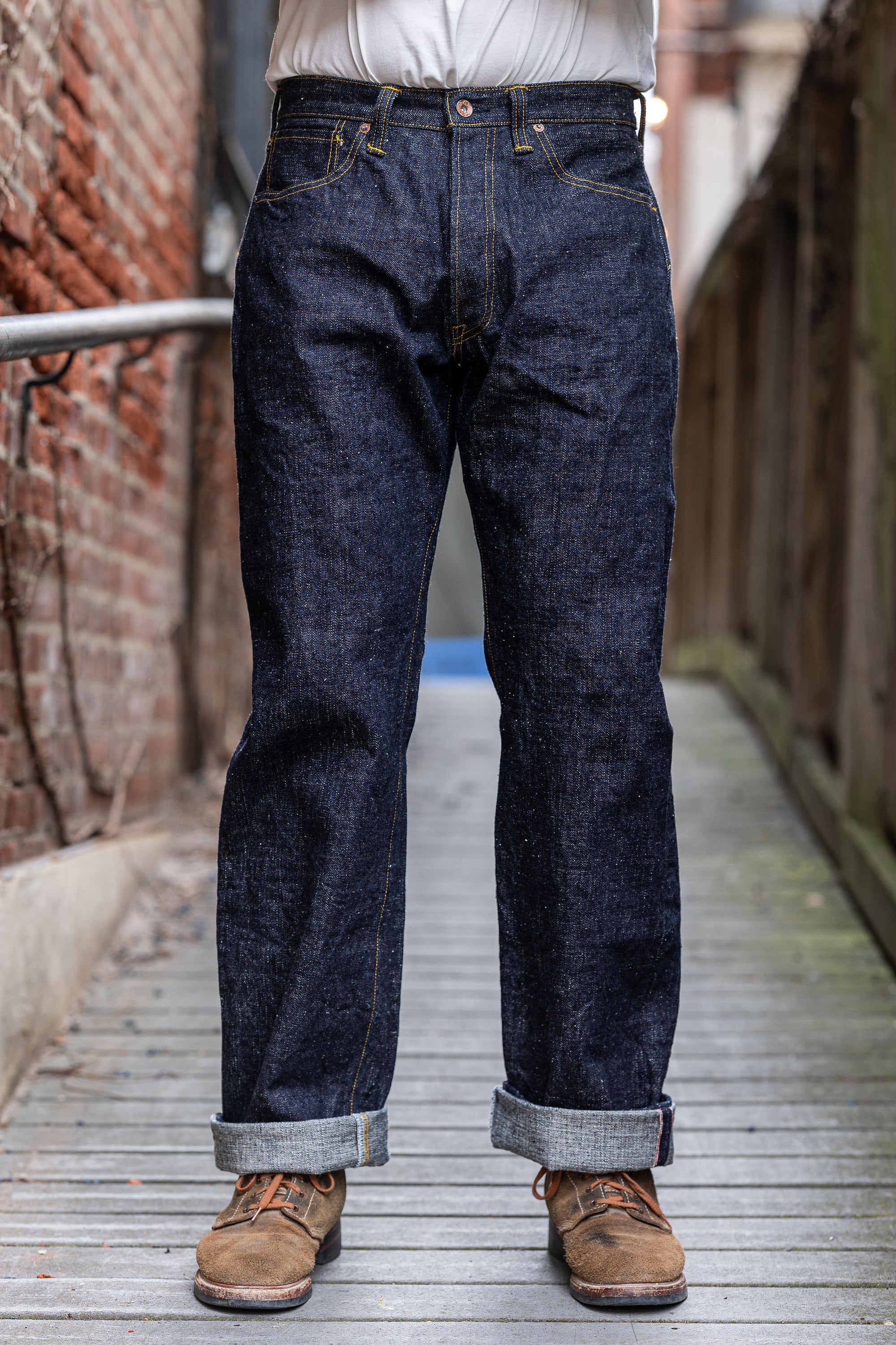 A person standing on a wooden platform wearing a pair of Samurai S3100VX 'Zero' WWII model wide straight jeans with a dark blue rinse.