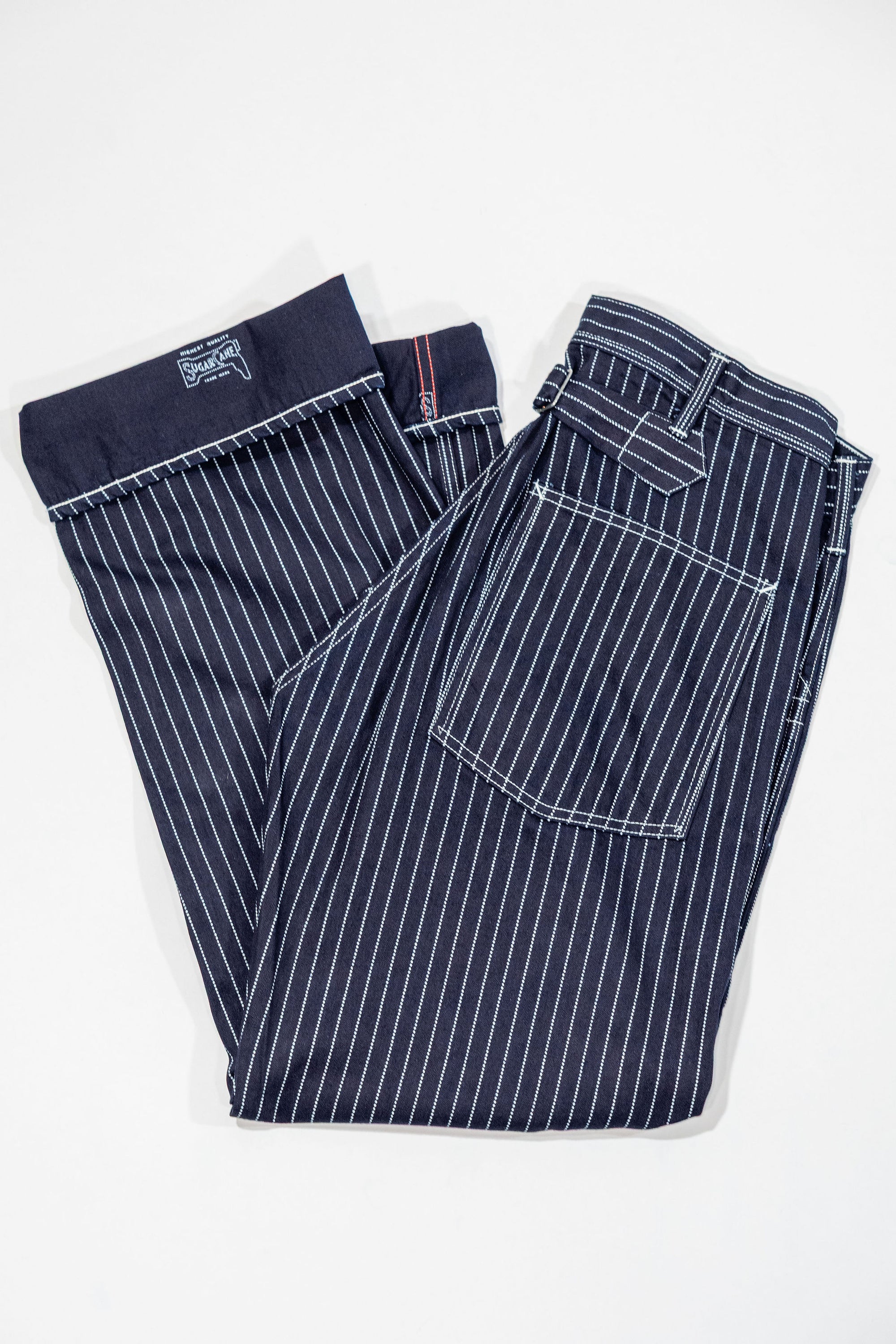 Navy striped fatigue pocket pants folded with hem cuffed to show solid navy interior and Sugar Cane branding, laying flat