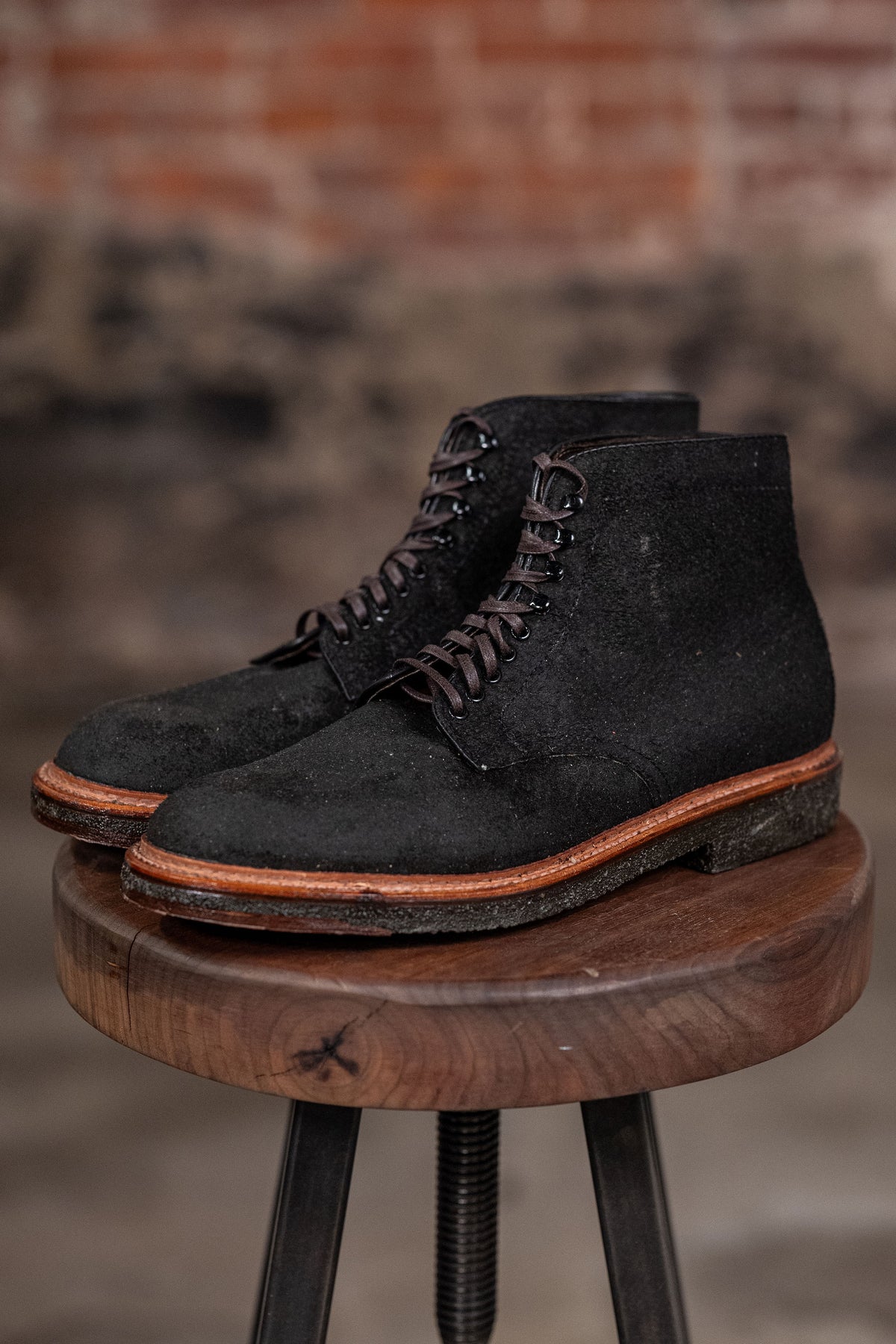 Alden Plain Toe boots on a wooden stool with a brick wall background - three quarter view