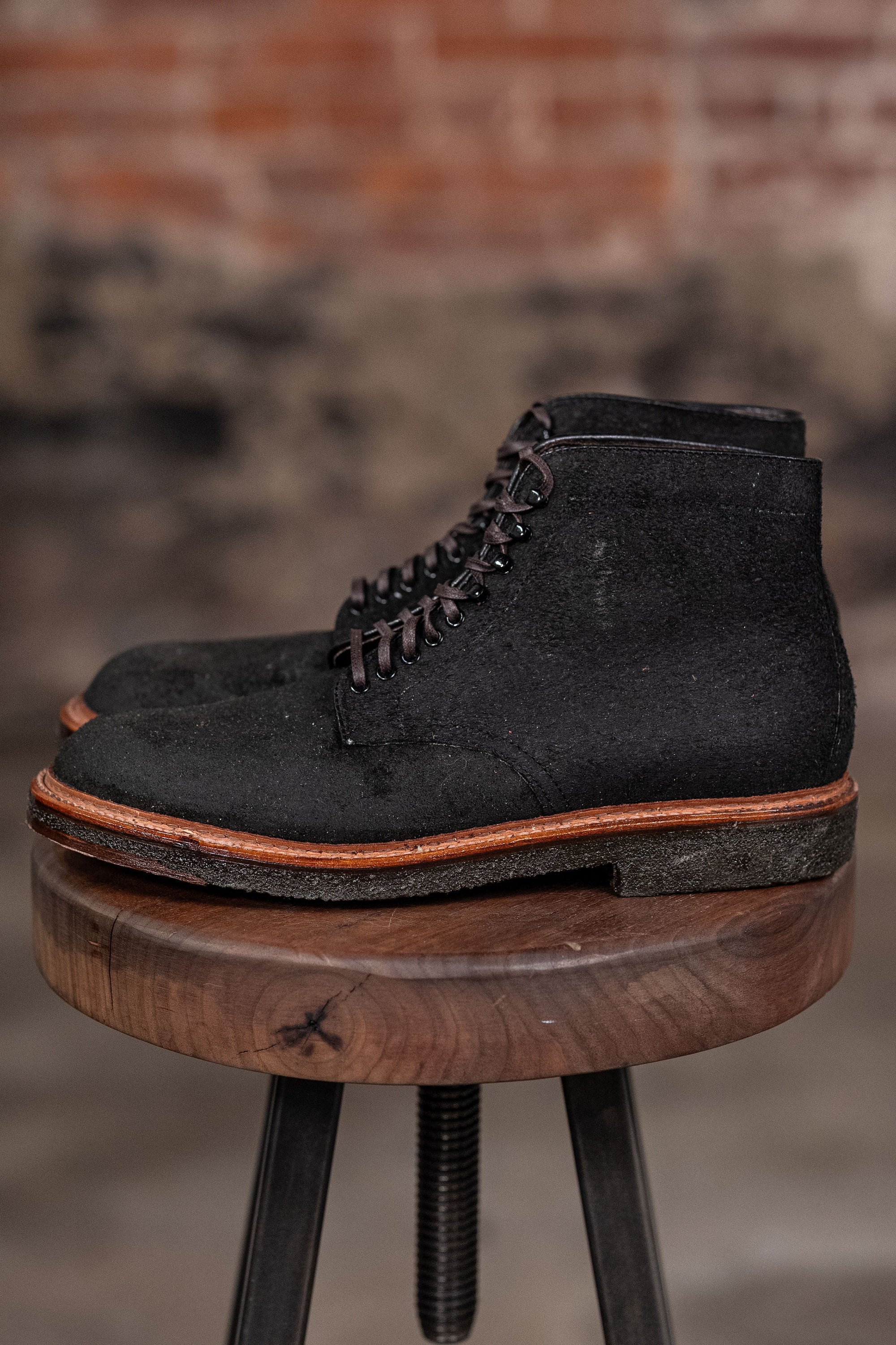 Alden Plain Toe boots on a wooden stool with a brick wall background - side view