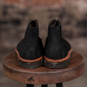 Pair of Alden Plain Toe boots on a wooden stool with a blurred brick wall background - back view