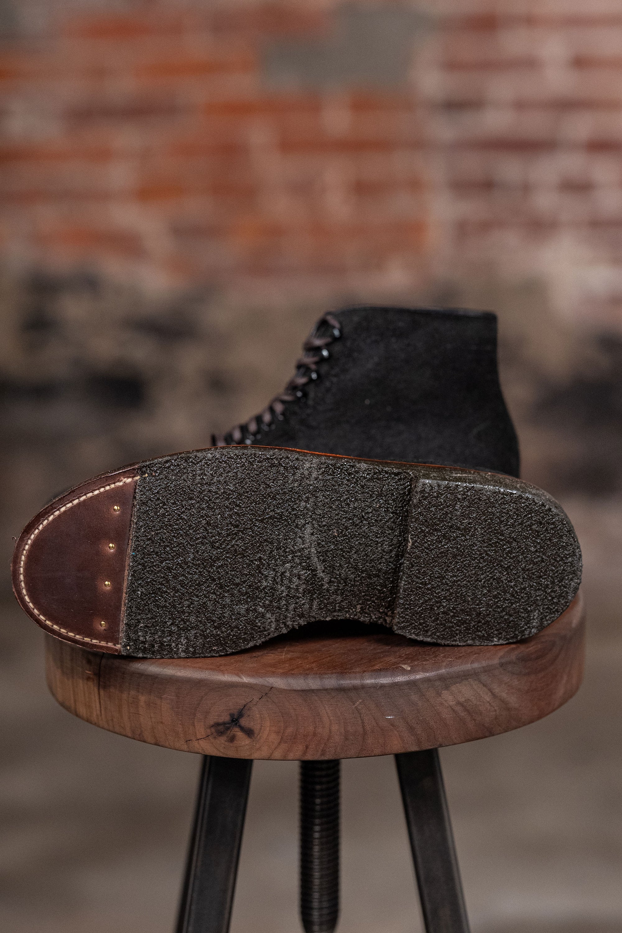 Alden Plain Toe boots on a wooden stool against a brick wall - view of sole
