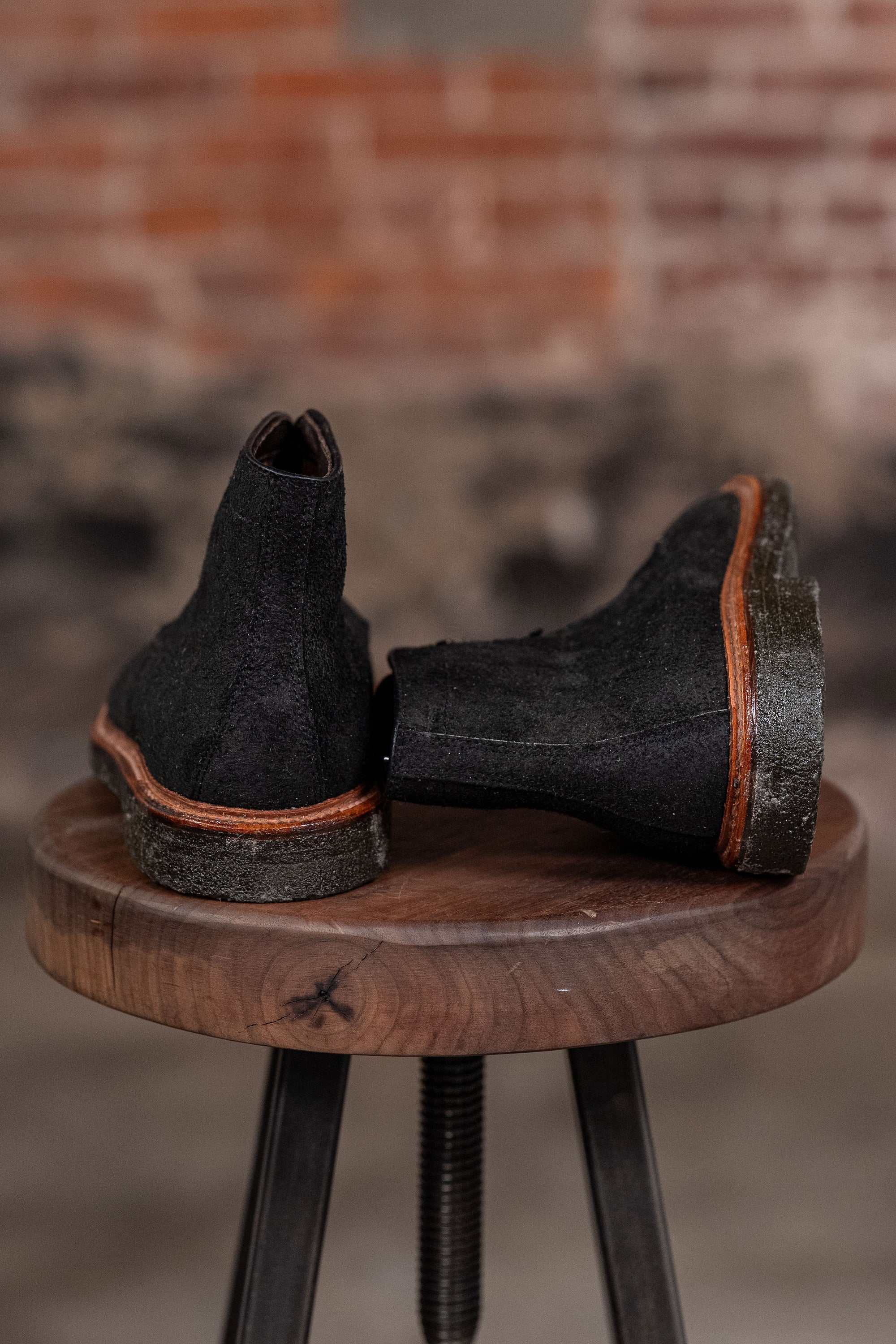 Pair of Alden Plain Toe boots on a wooden stool with a blurred background - back view
