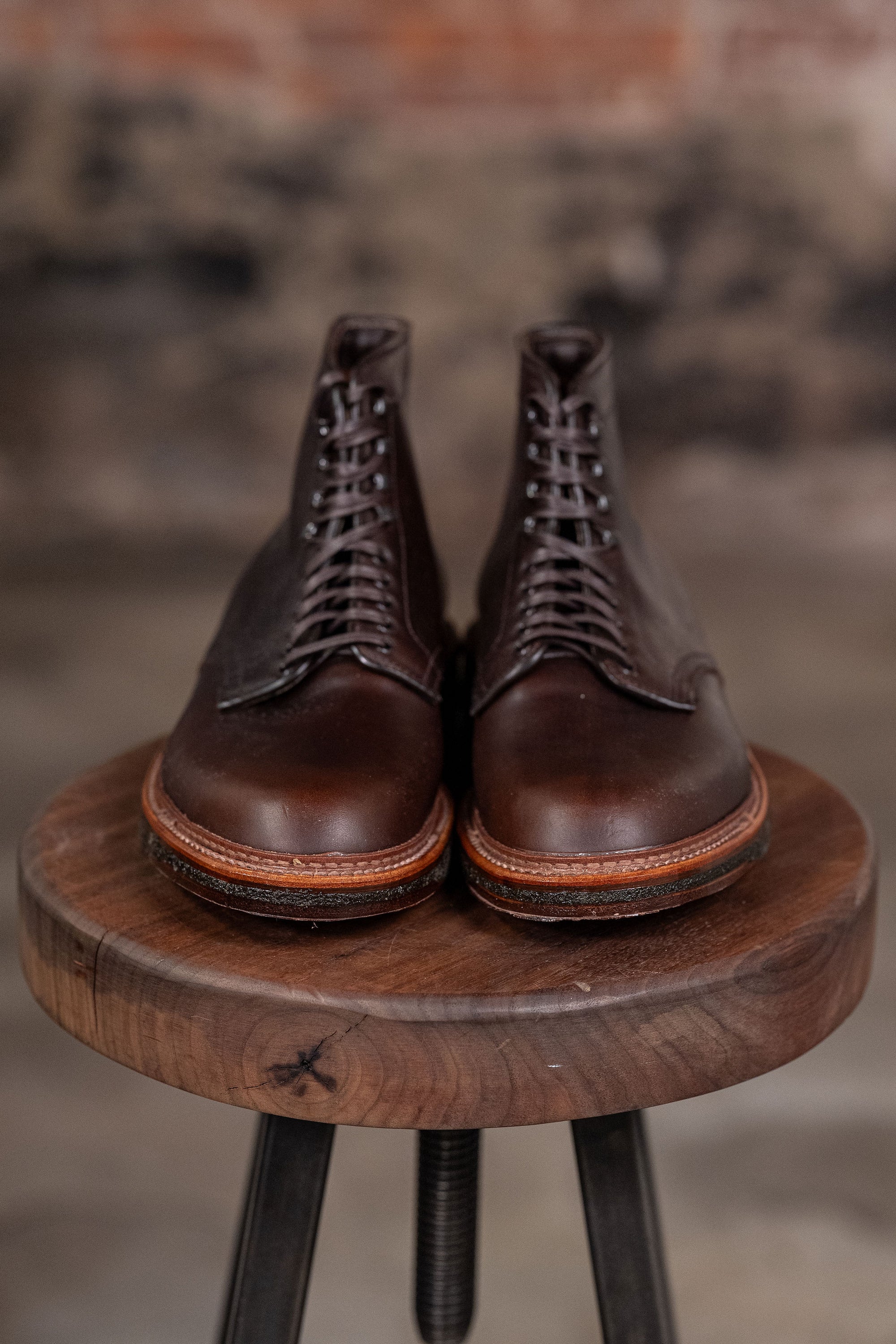 Pair of Alden Plain Toe boots on a wooden stool with a blurred background - front view