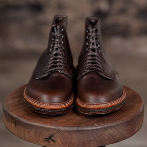 Pair of Alden Plain Toe boots on a wooden stool with a blurred background - front view
