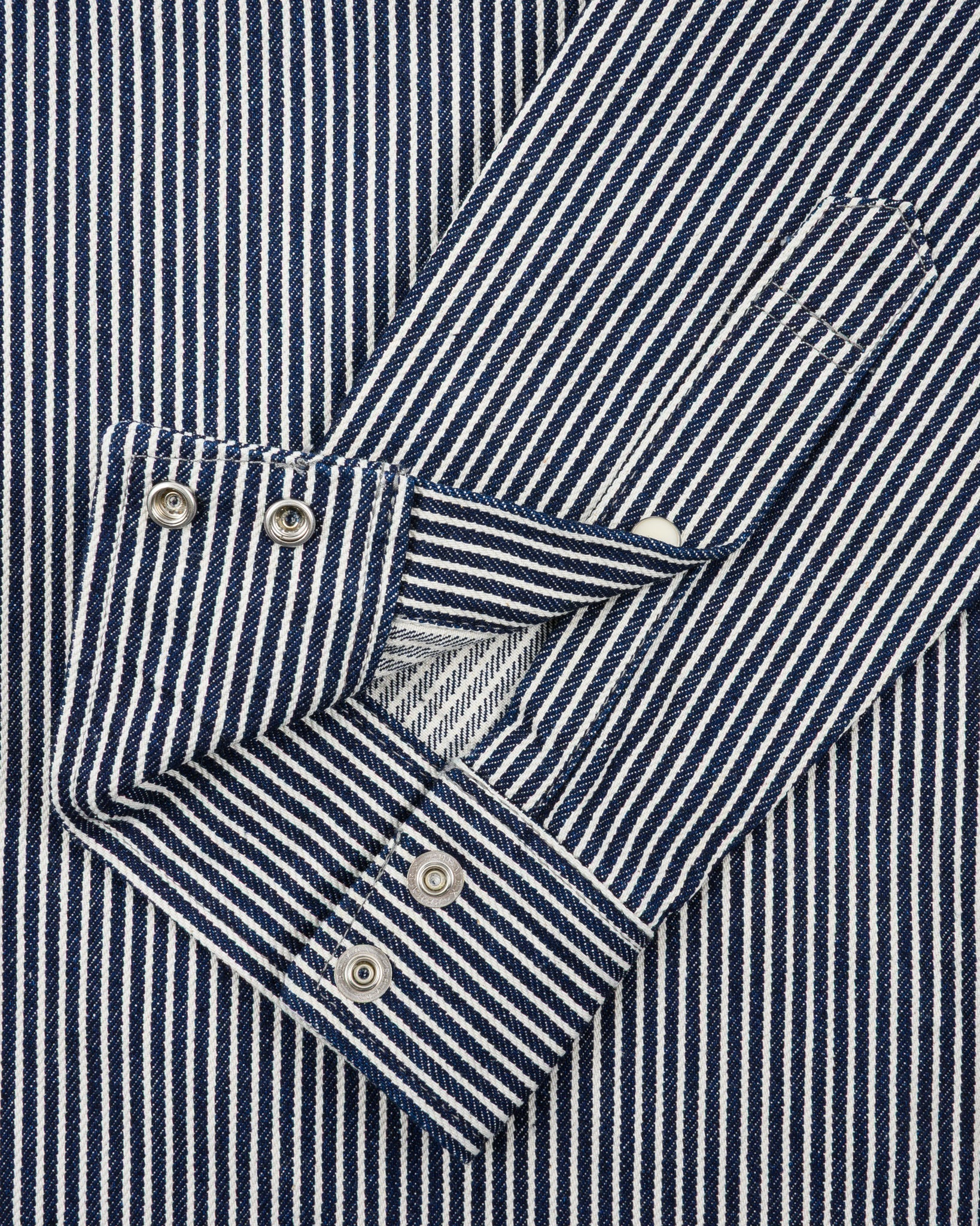 Western style shirt with indigo and white thin vertical stripes and white snaps close-up on sleeve unbuttoned