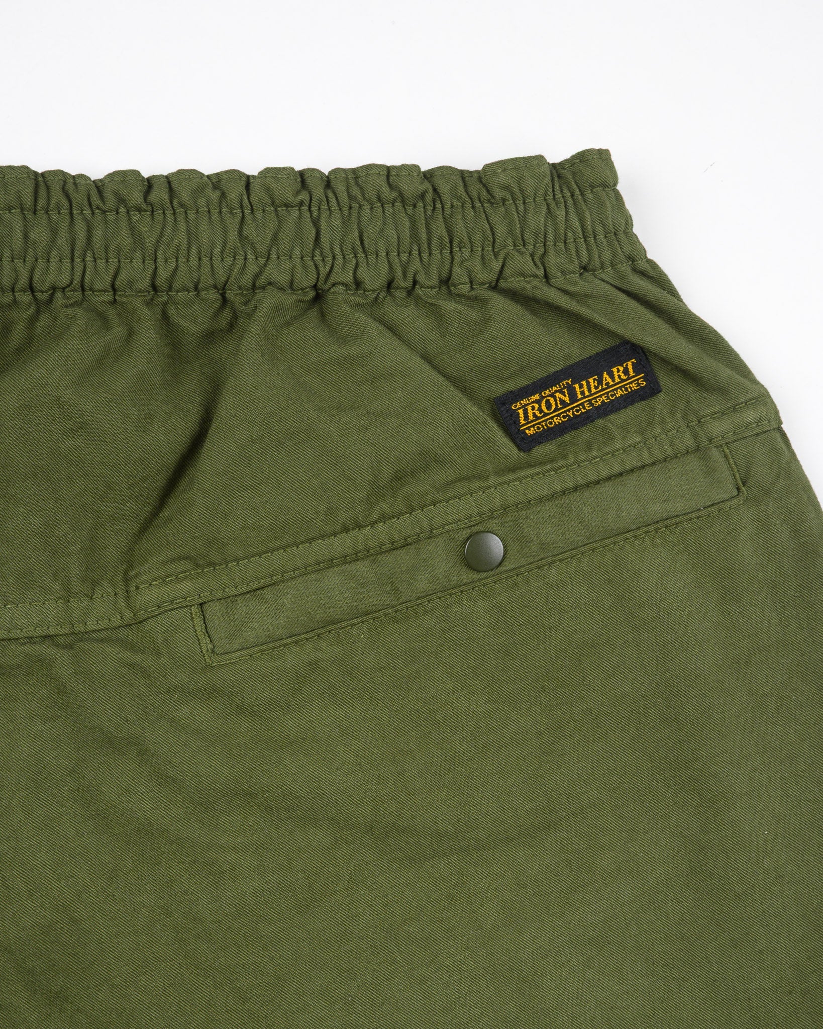 Olive mid length shorts back view laying flat closeup on snap pocket and black/yellow Iron Heart logo