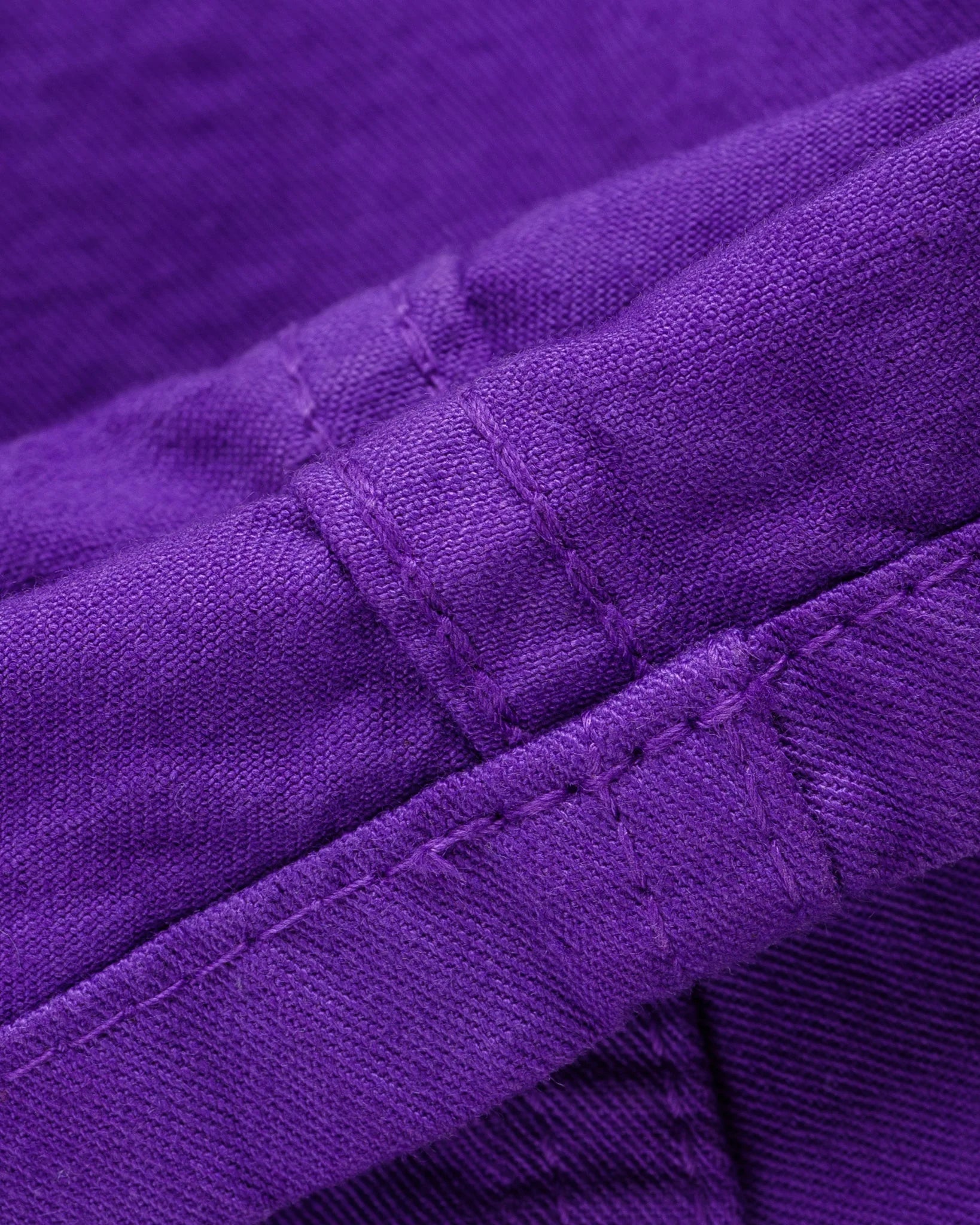 Purple mid length shorts laying flat closeup on stitching