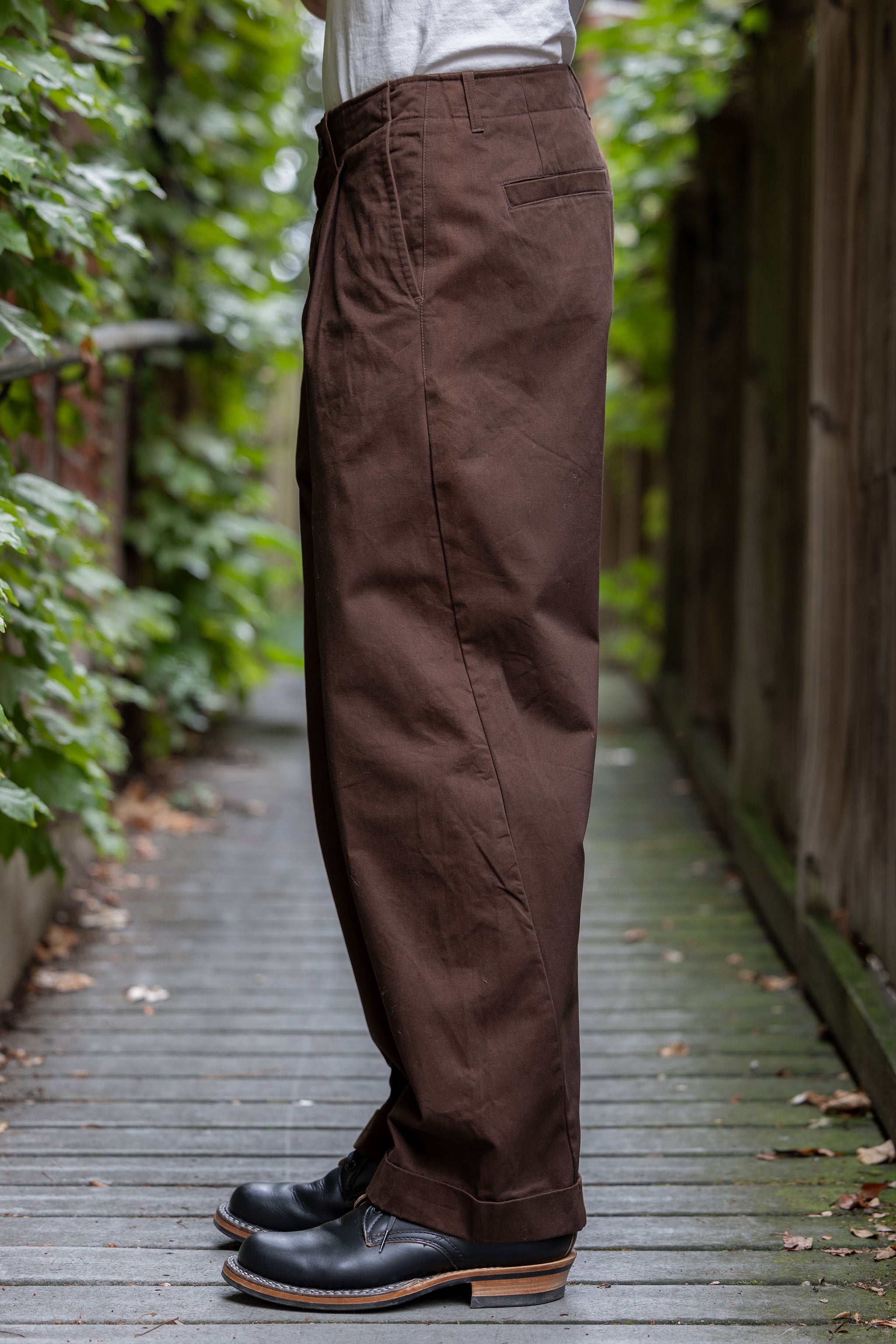 Hansen Garments Bobby Wide Pleated Trousers - Chestnut - model shot - side facing - foliage alleyway background