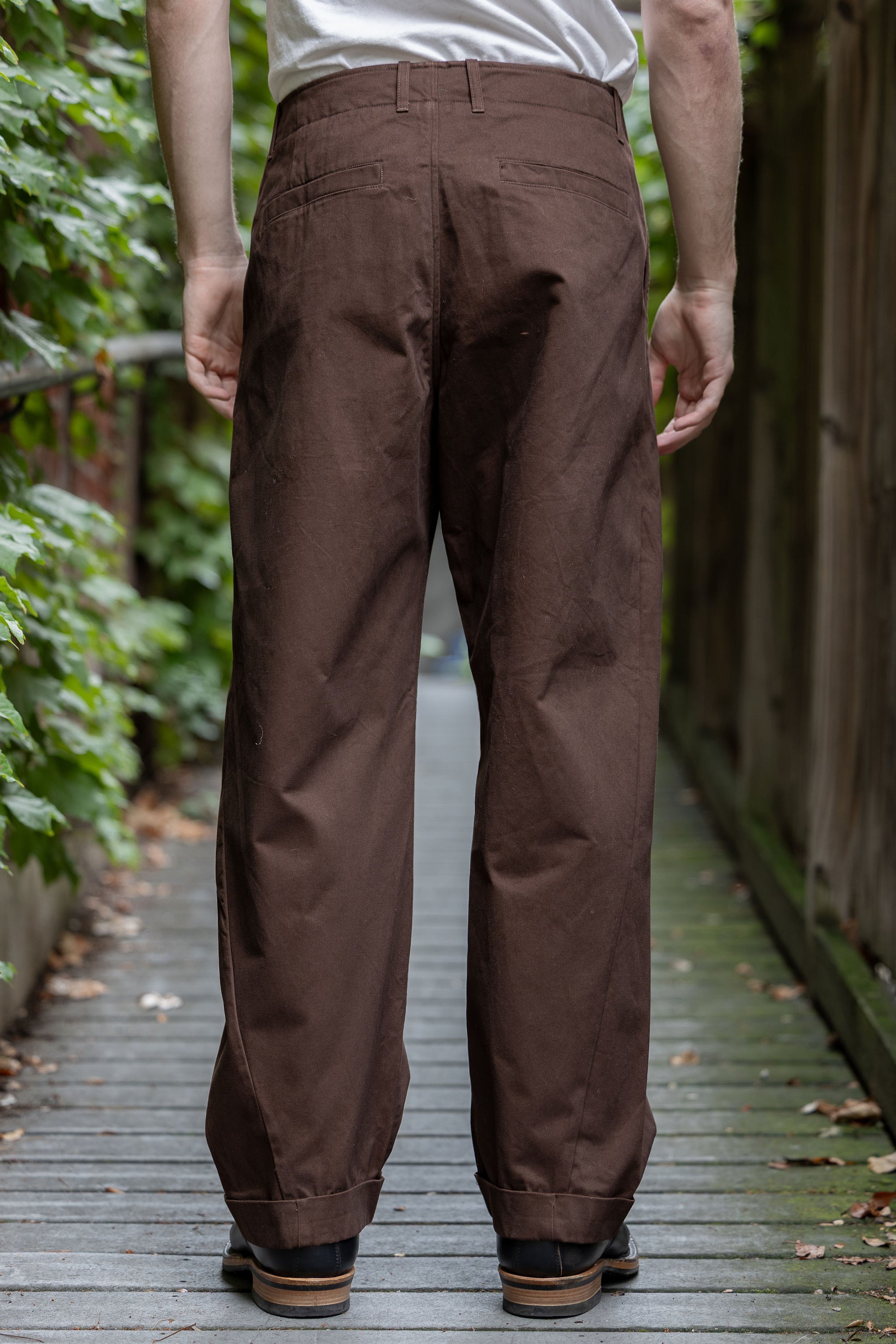 Hansen Garments Bobby Wide Pleated Trousers - Chestnut - model shot - back facing - foliage alleyway background
