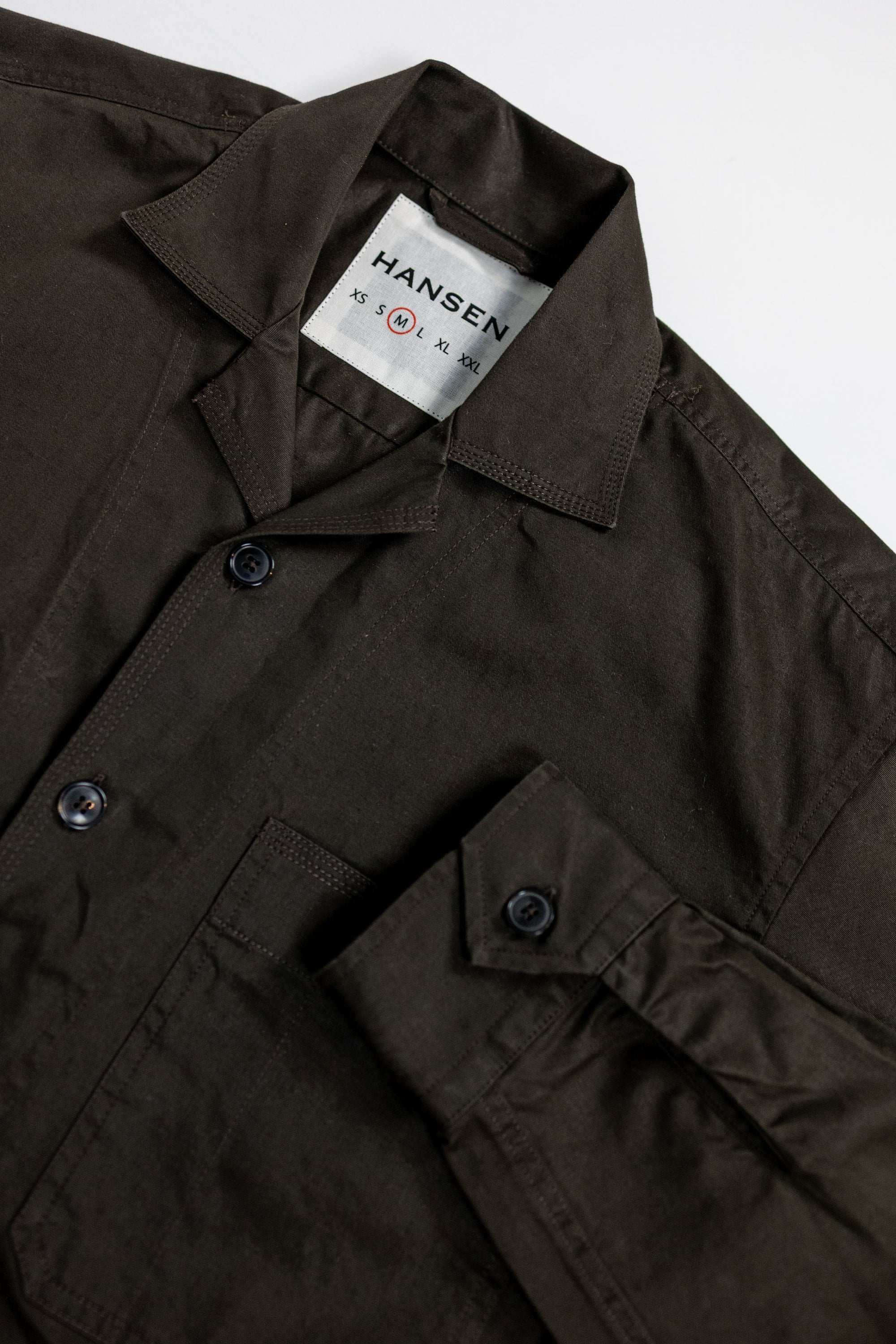 Hansen Garments Steffen Shirt Jacket - Coffee Drill - product shot - front facing - white background - detail shot of collar, button, sleeve, and brand tag