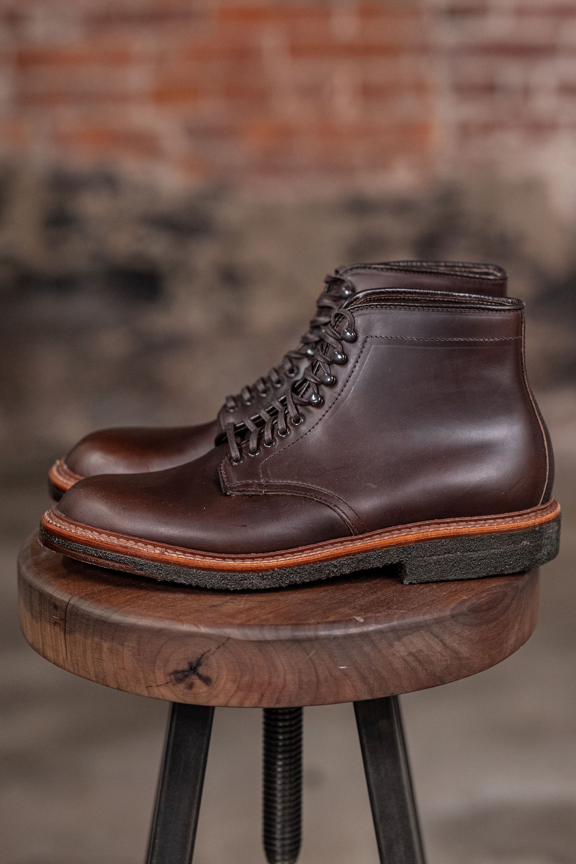 Alden Plain Toe boots on a wooden stool with a brick wall background - side view
