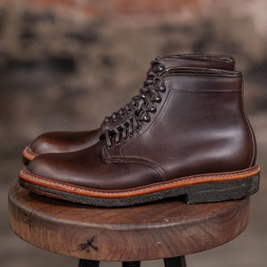 Alden Plain Toe boots on a wooden stool with a brick wall background - side view