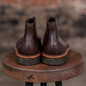 Pair of Alden Plain Toe boots on a wooden stool with a blurred brick wall background - back view