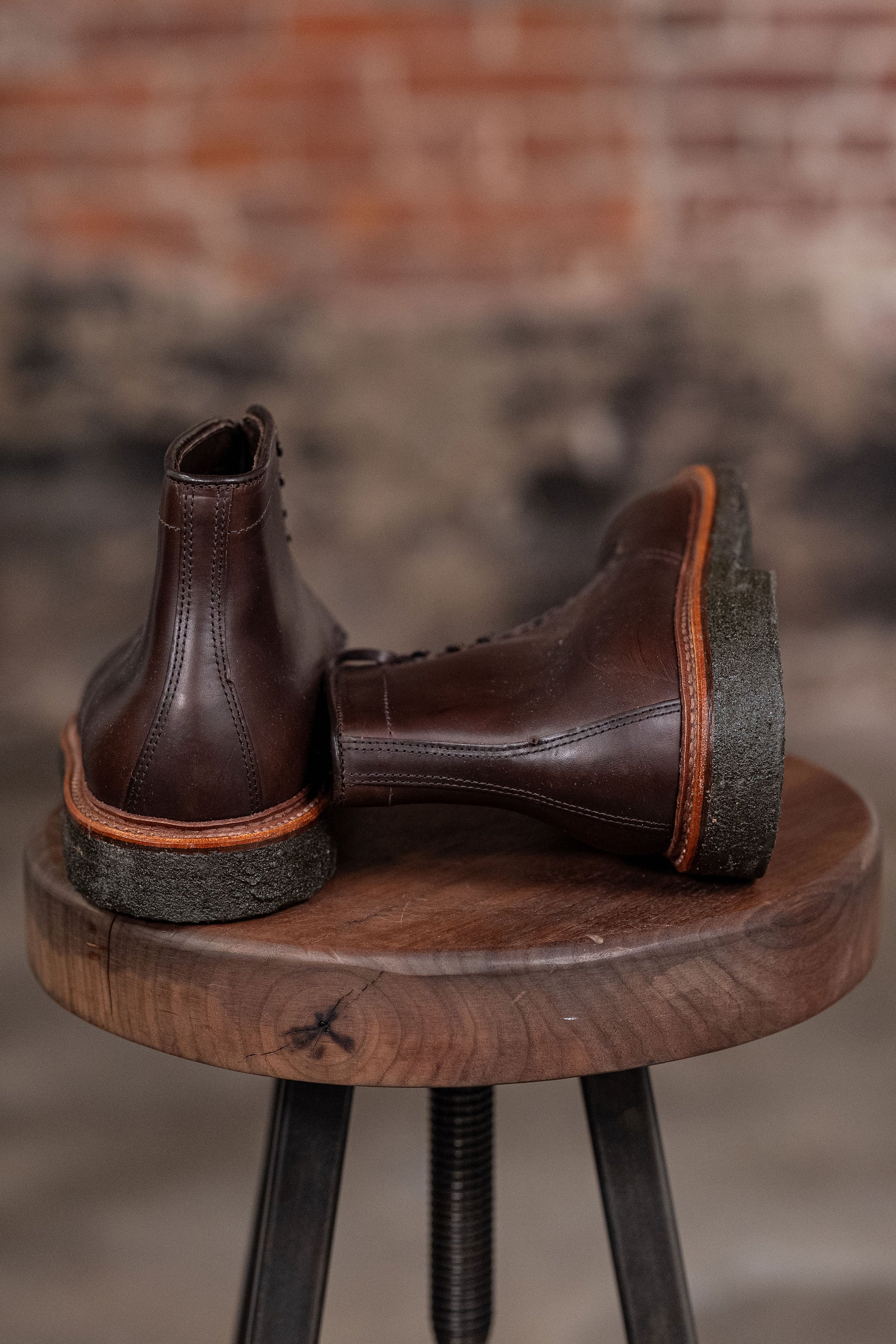 Pair of Alden Plain Toe boots on a wooden stool with a blurred background - back view