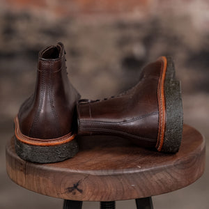 Pair of Alden Plain Toe boots on a wooden stool with a blurred background - back view