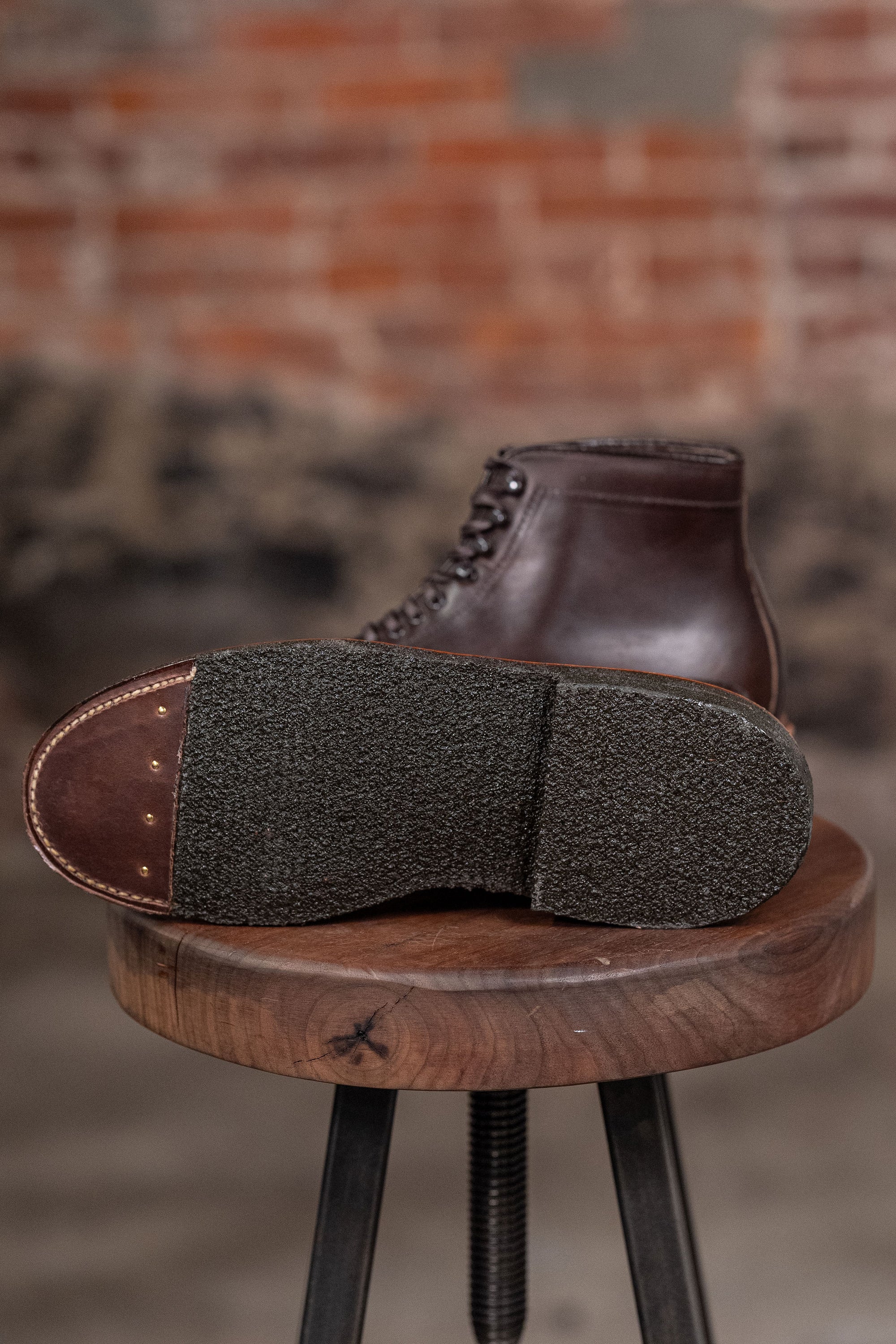 Alden Plain Toe boots on a wooden stool against a brick wall - view of sole
