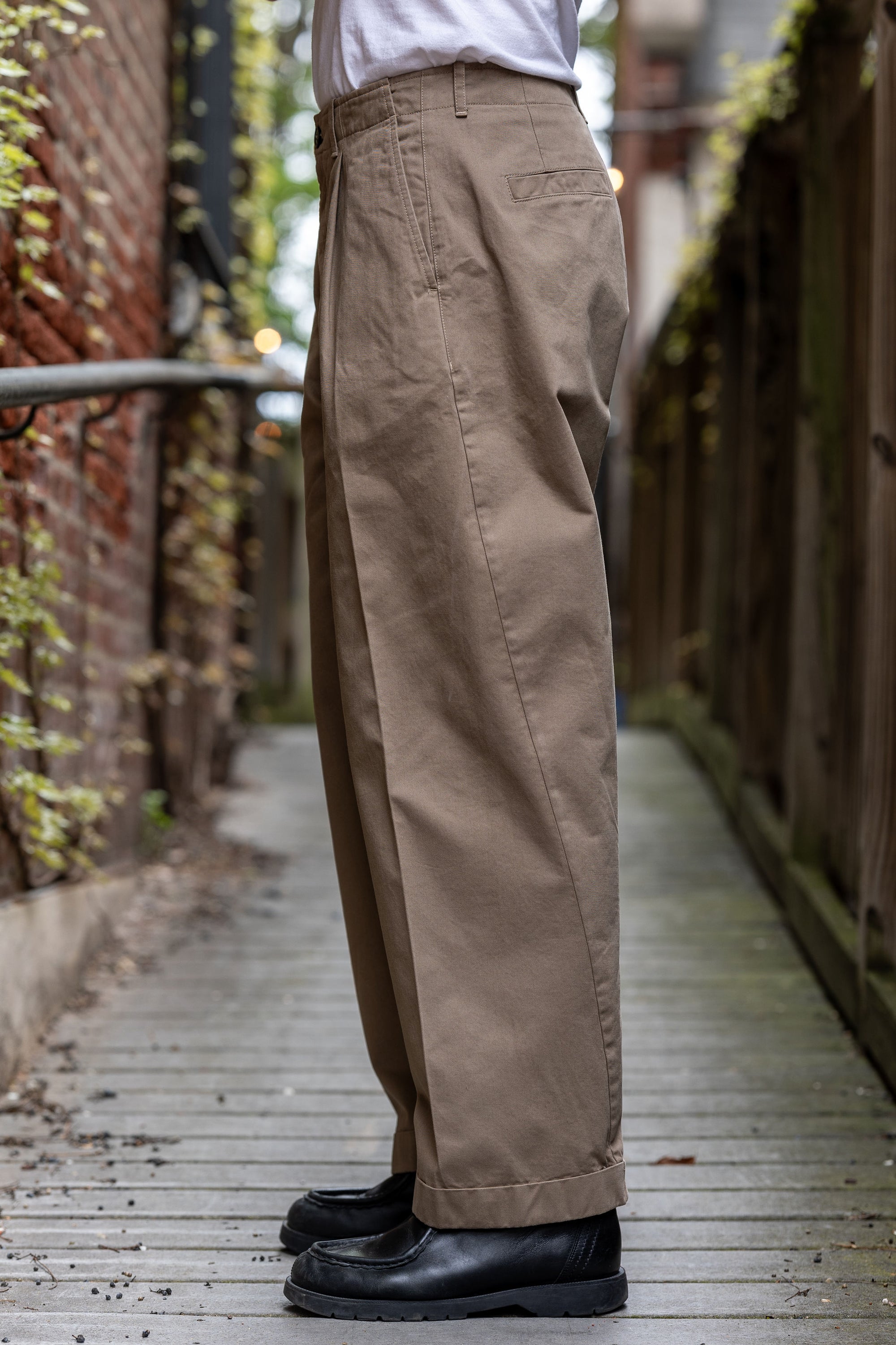 Hansen Garments Bobby Wide Pleated Trousers - Beige - model shot - waist down - side facing - wooden alley background