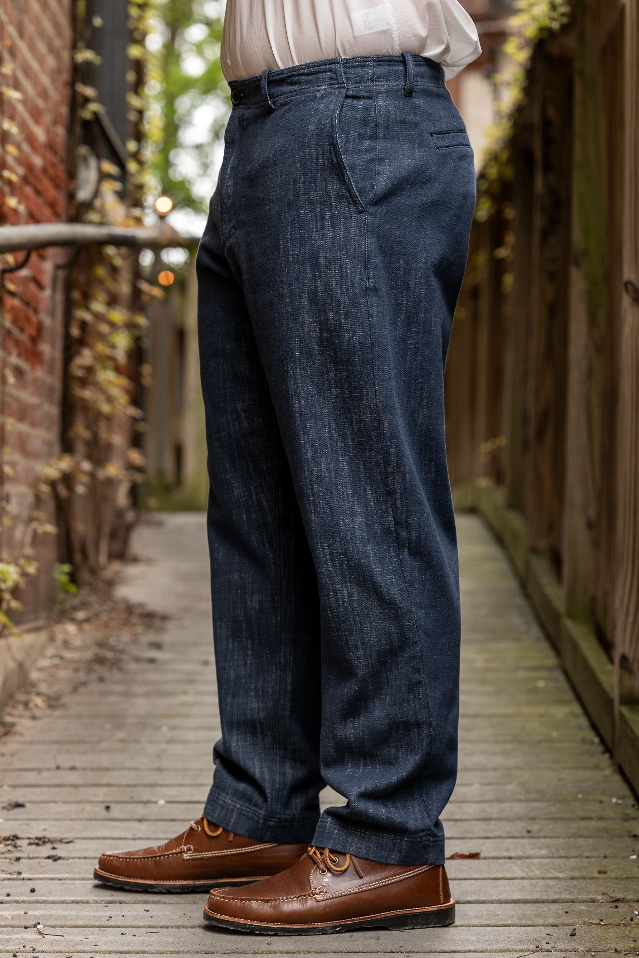 Hansen Garments Trygve Wide Cut Cropped Trousers - Denim Blue - model shot - waist down - side facing - brick & wood alleyway background