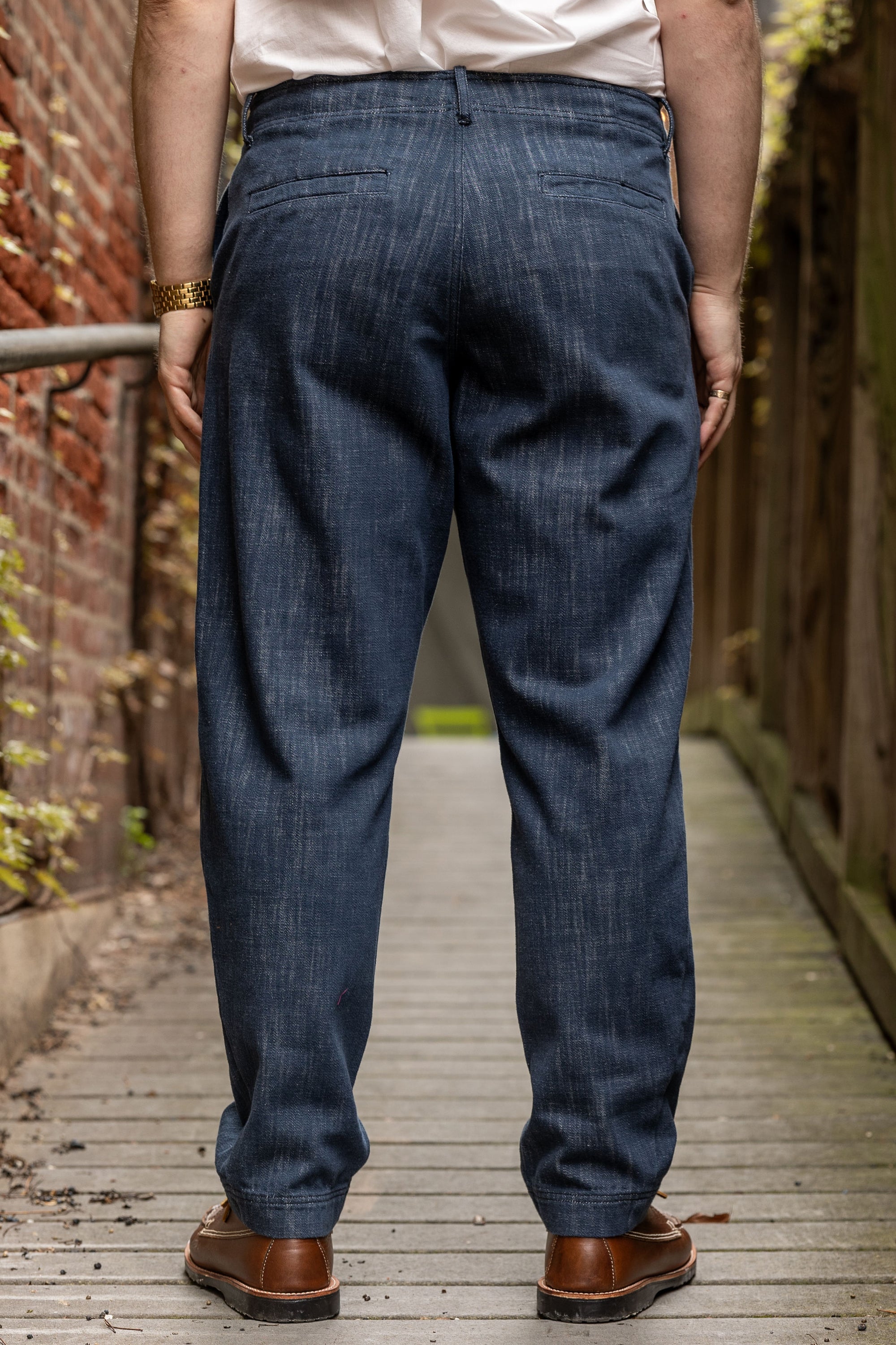 Hansen Garments Trygve Wide Cut Cropped Trousers - Denim Blue - model shot - waist down - back facing - brick & wood alleyway background