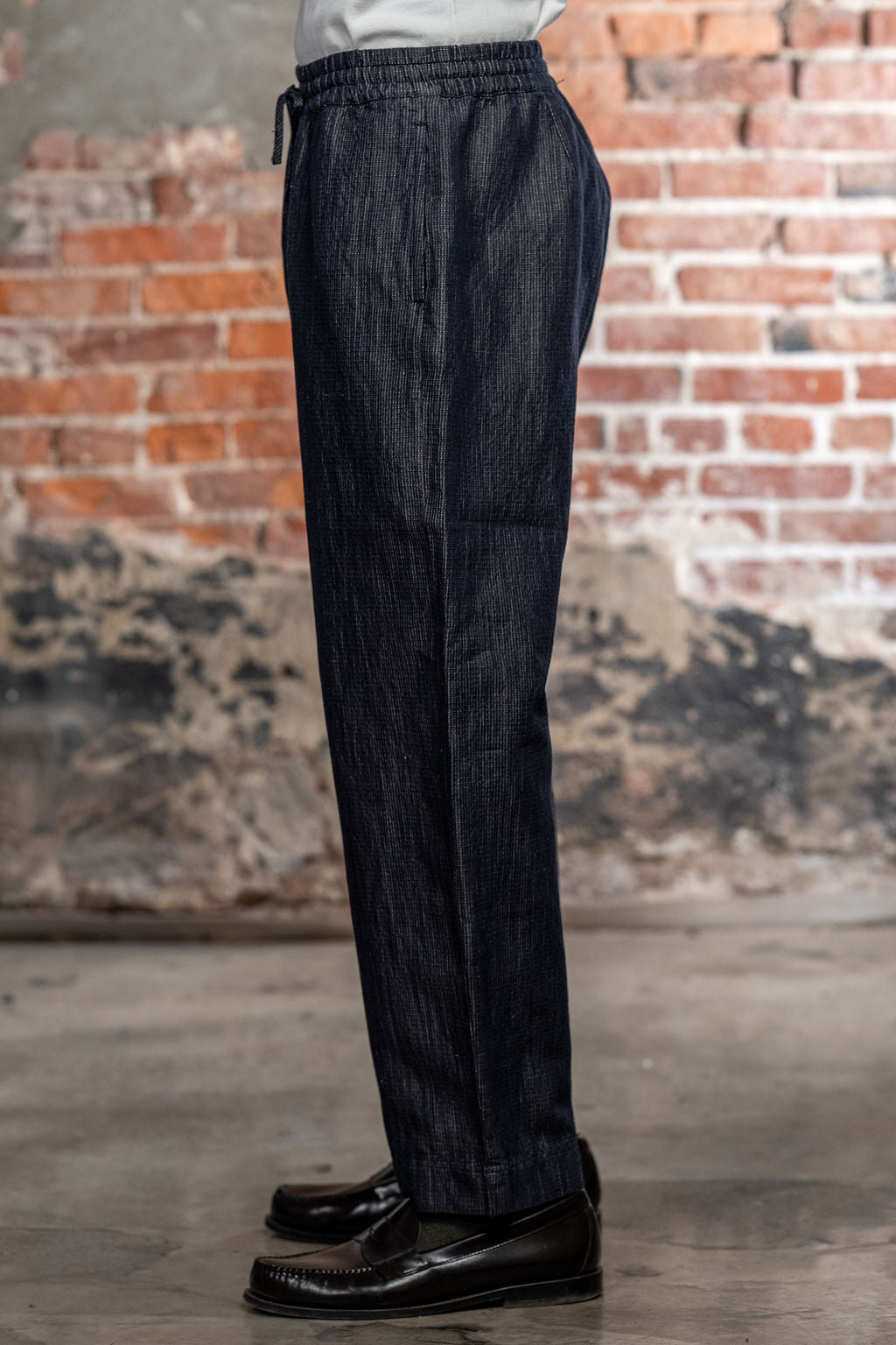 Hansen Garments Emir Loose Drawstring Pants - Navy Dobby - close up - waist down - brick background - side facing