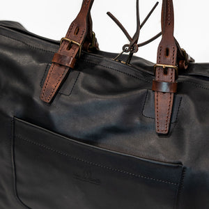 Black leather duffel bag with pockets and brown leather handles front view closeup
