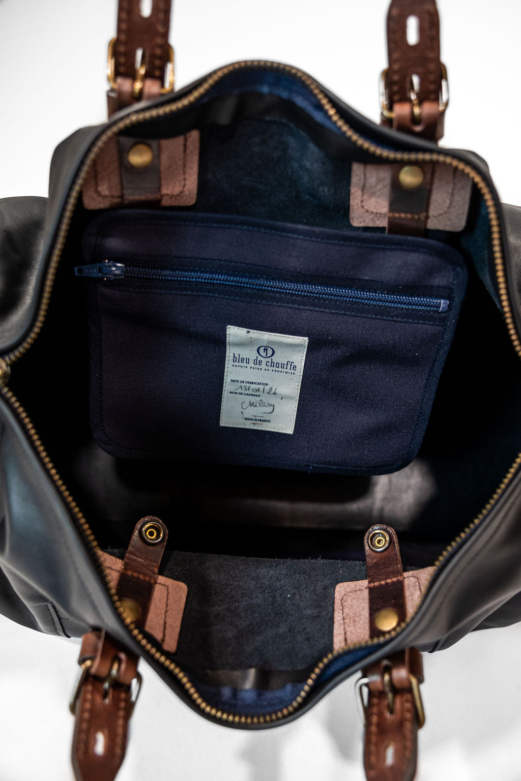 Black duffel bag with brown handles closeup on navy internal lining and pocket with white label