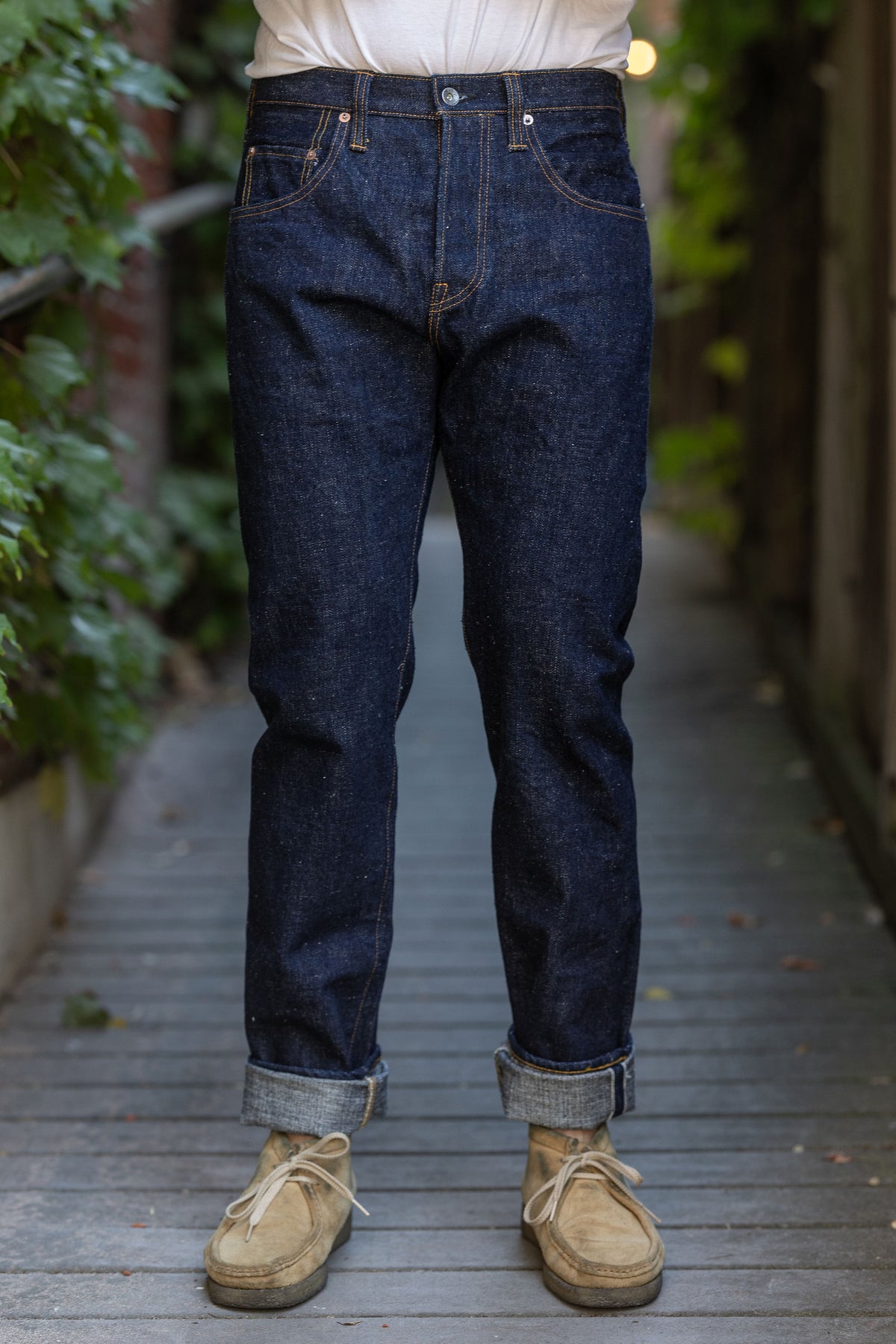 A person standing on a wooden pathway wearing Samurai S211AX Ai Benkei 18oz Natural Indigo Relaxed Tapered Denim jeans and beige shoes.