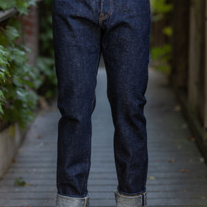A person standing on a wooden pathway wearing Samurai S211AX Ai Benkei 18oz Natural Indigo Relaxed Tapered Denim jeans and beige shoes.