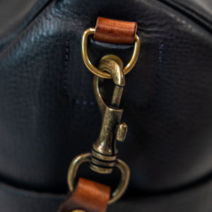Black leather duffel bag with pockets and brown leather handles closeup on strap trigger hook