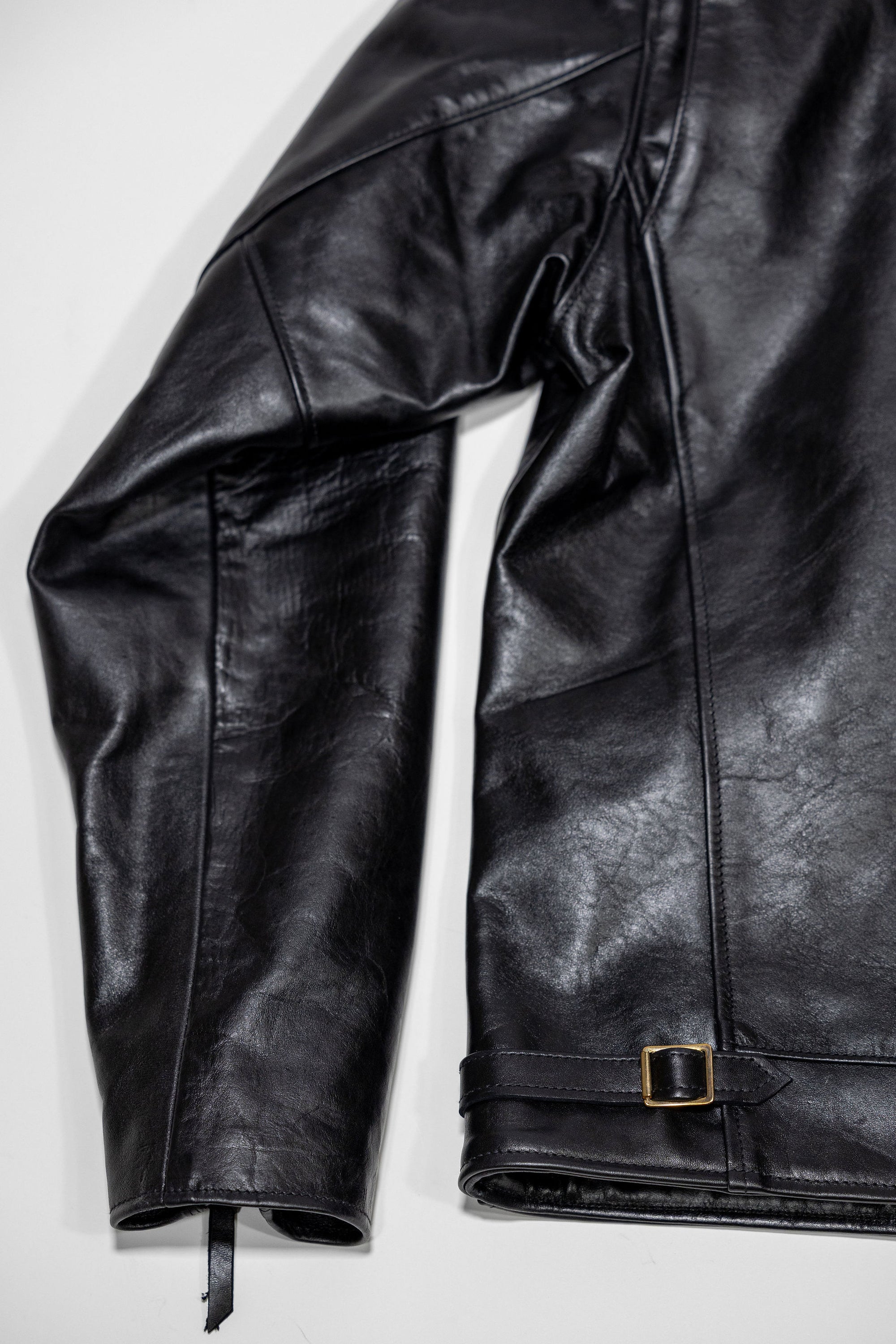 Black leather jacket laid flat on white. Details on back of sleeve and bottom of jacket 