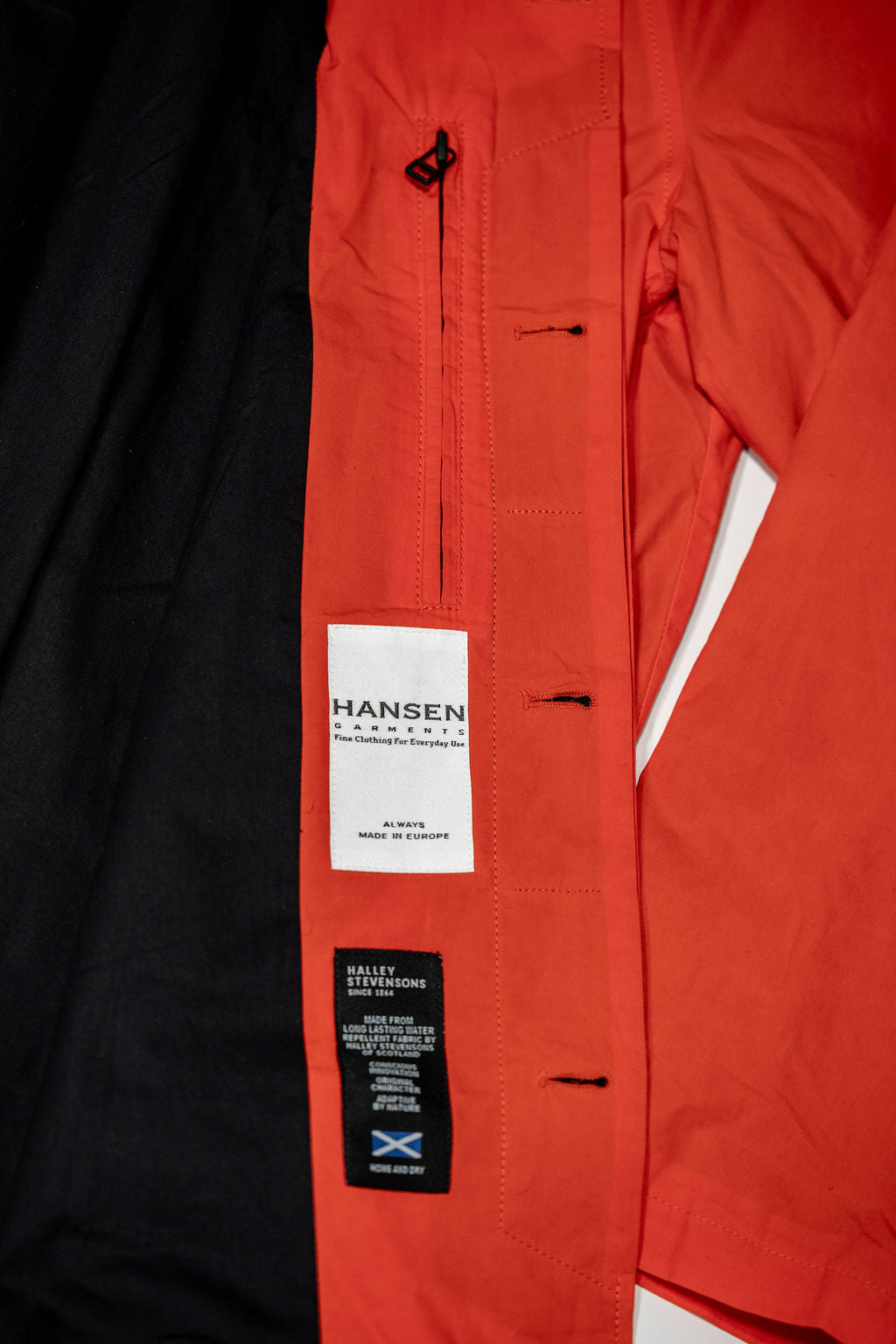 Hansen Garments Morten Long Coat - Waxed Orange laid flat. Details on buttons holes