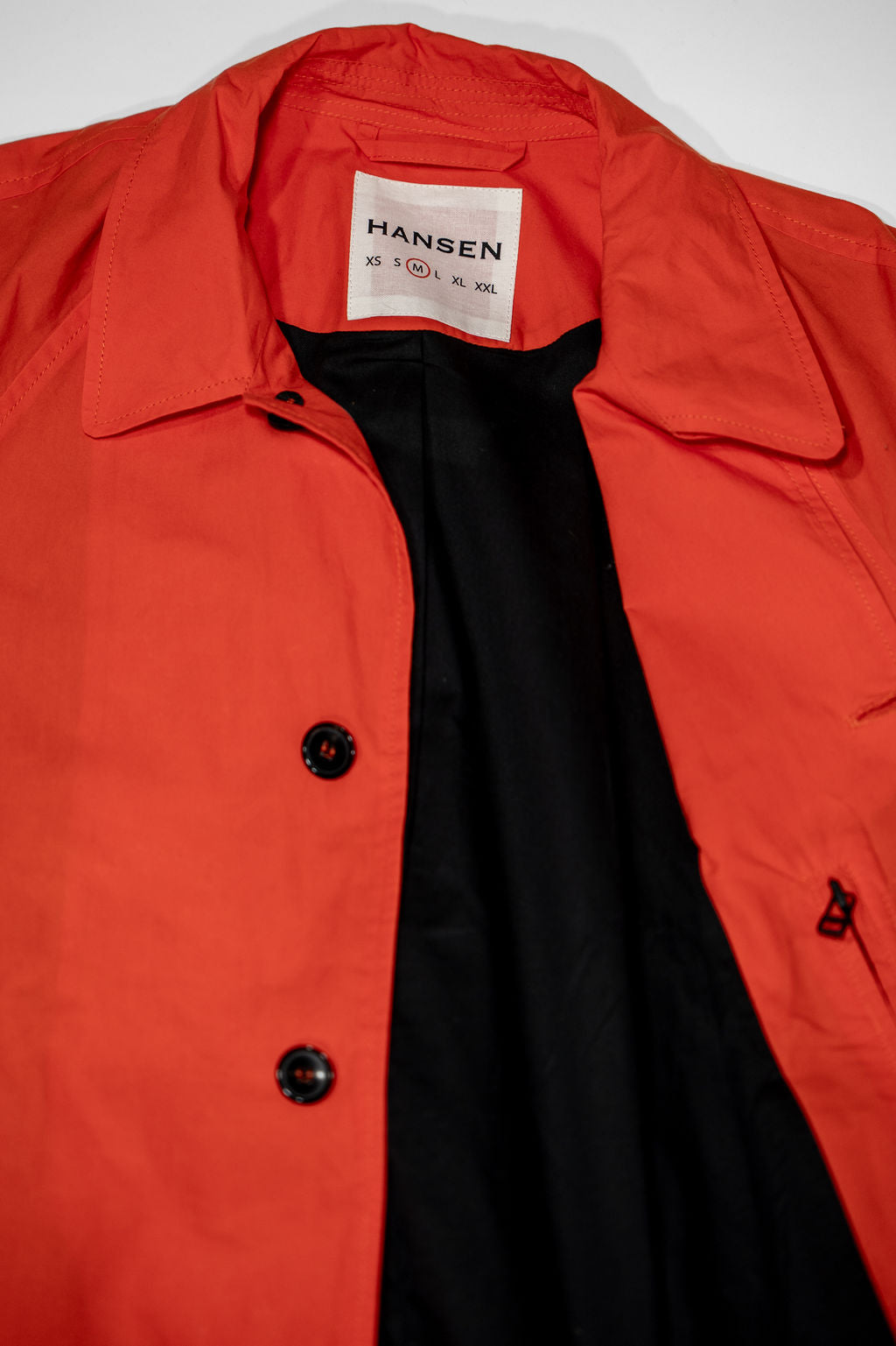 Hansen Garments Morten Long Coat - Waxed Orange laid flat. Details on buttons and open collar