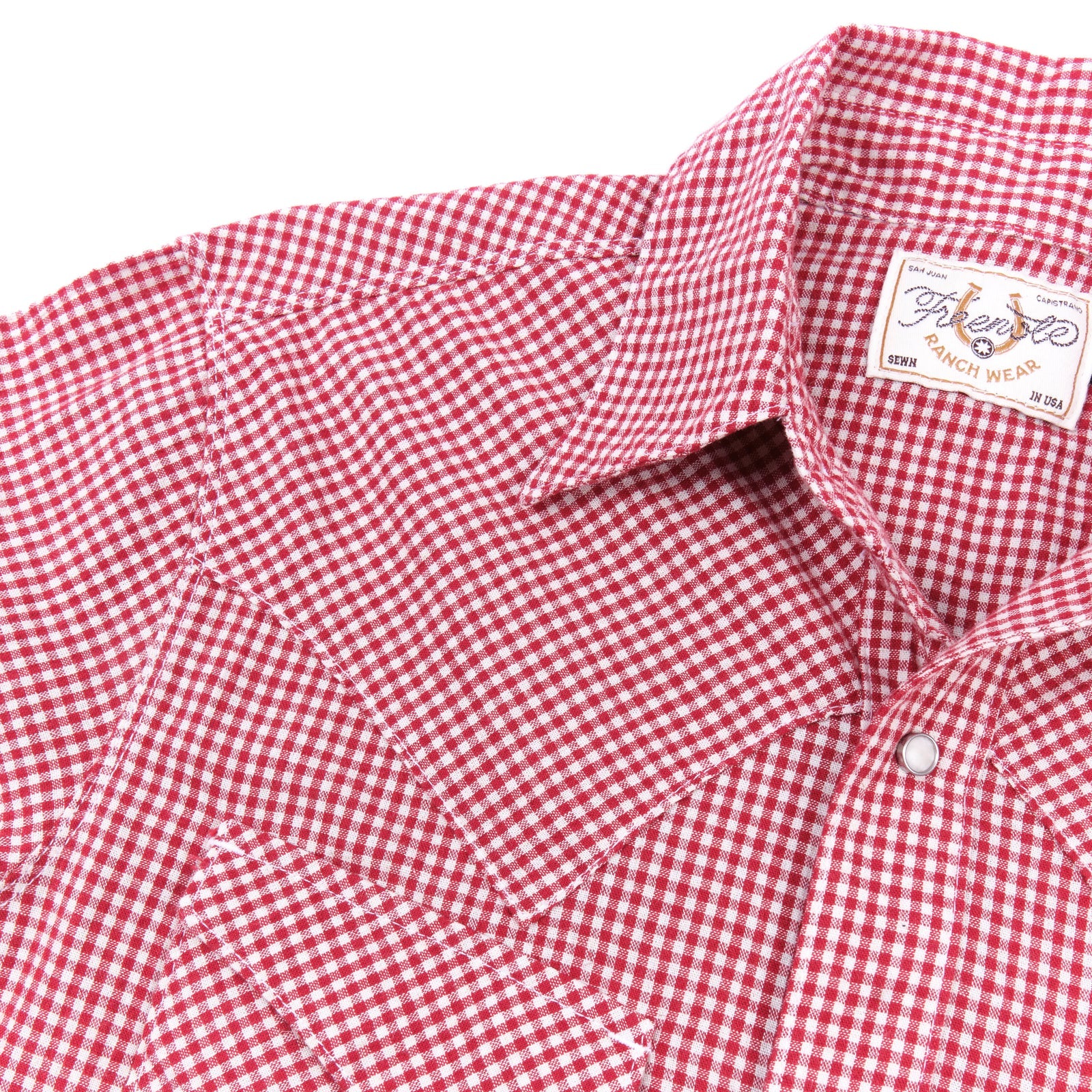 Red and white gingham western-style button-down shirt with two buttoned chest pockets, close up on shoulder laying flat