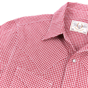 Red and white gingham western-style button-down shirt with two buttoned chest pockets, close up on shoulder laying flat