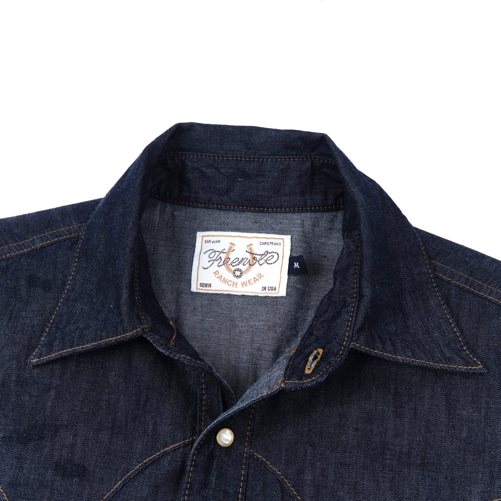 Dark indigo denim western-style shirt with white snaps, close up on collar laying flat