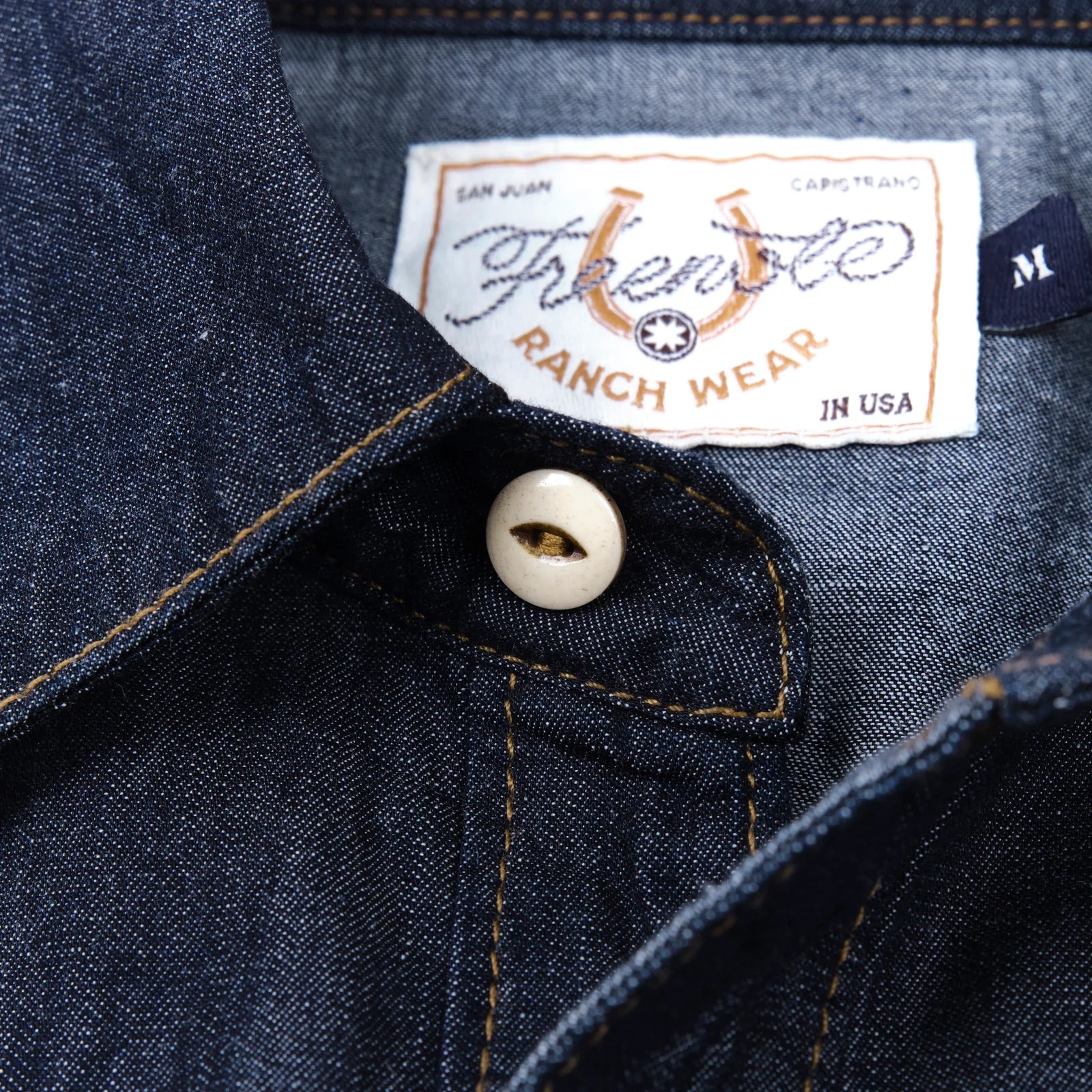 Dark indigo denim western-style shirt with white snaps, close up on top button laying flat