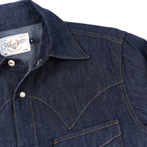 Dark indigo denim western-style shirt with white snaps, close up on shoulder laying flat