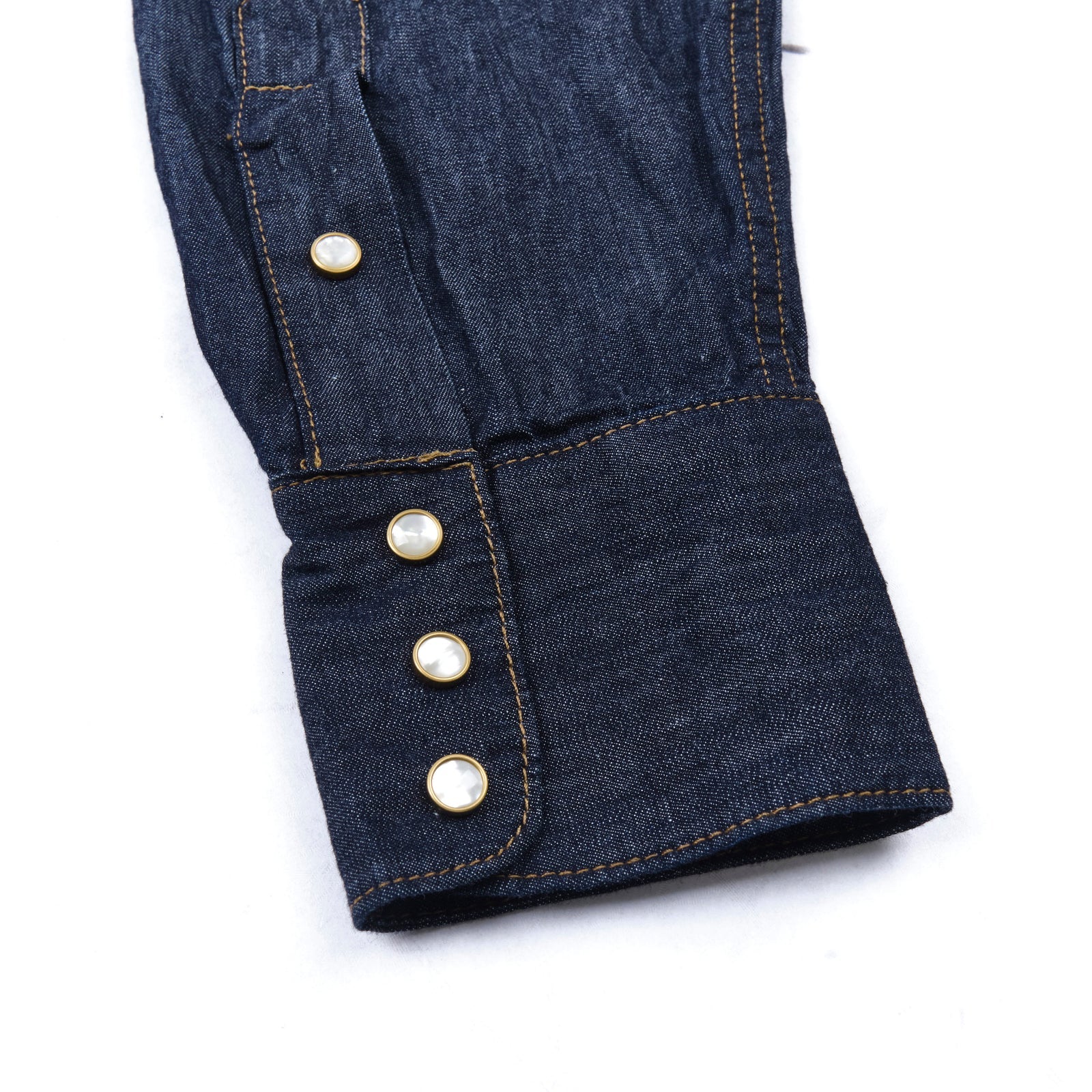 Dark indigo denim western-style shirt with white snaps, close up on sleeve cuff laying flat