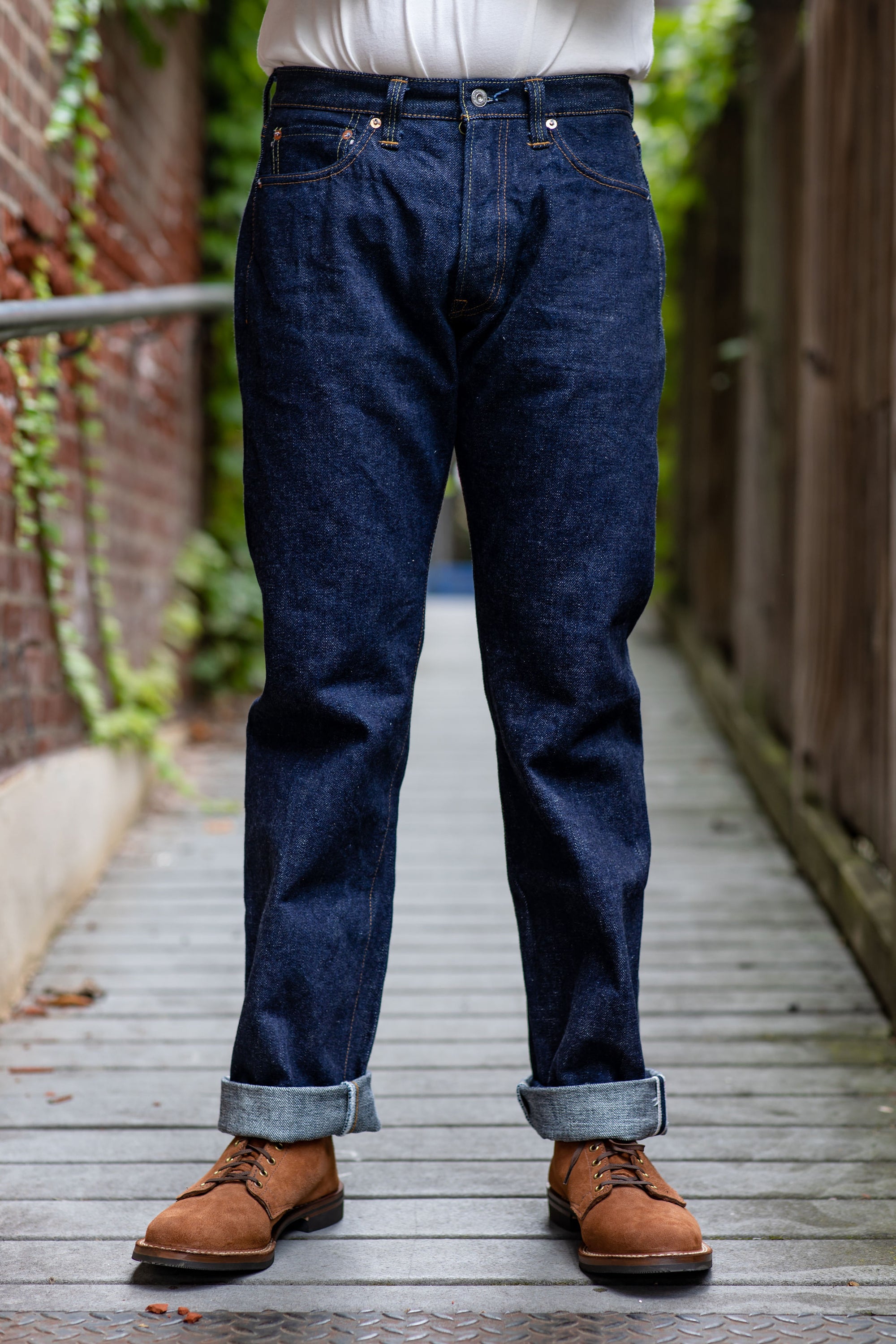 A person standing on a pathway wearing Samurai S510XX21ozII 21oz Cho-Kiwami Selvedge Regular Straight denim jeans in one wash, paired with brown shoes.